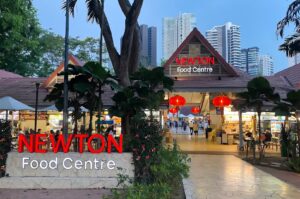 Main entrance of the famous Newton Food Centre in Singapore, featuring red lanterns and illuminated signage against a dusk skyline.