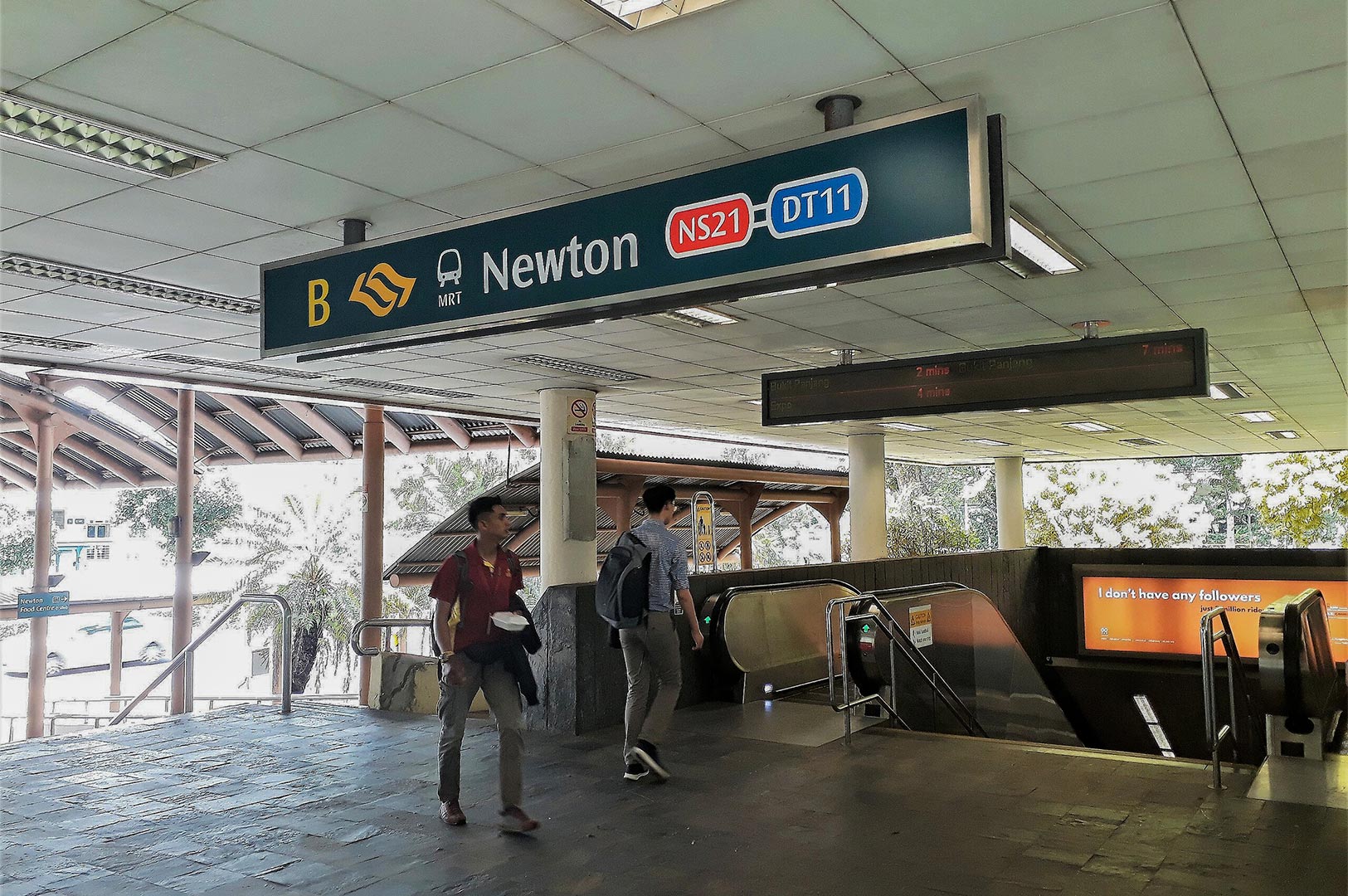 Commuters walking near Exit B of Newton MRT station in Singapore, displaying signage for the North-South (NS21) and Downtown (DT11) lines.