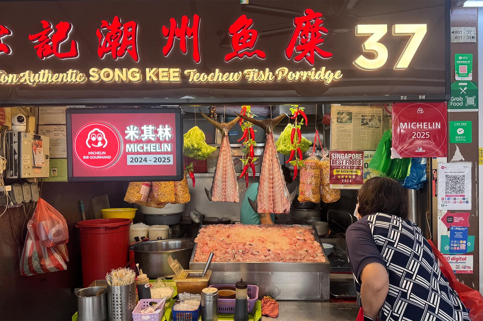 Storefront of Song Kee Teochew Fish Porridge at Newton Food Centre, displaying a red Michelin Bib Gourmand 2024-2025 recognition sign and fresh ingredients.