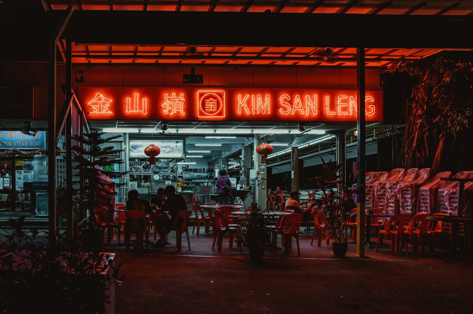 Bright neon sign illuminating the area, representing a Singaporean hawker food stall.