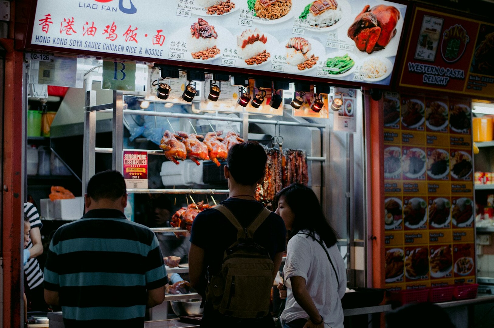 People standing in front of a Singapore hawker food stall, showcasing the lively atmosphere of local cuisine.