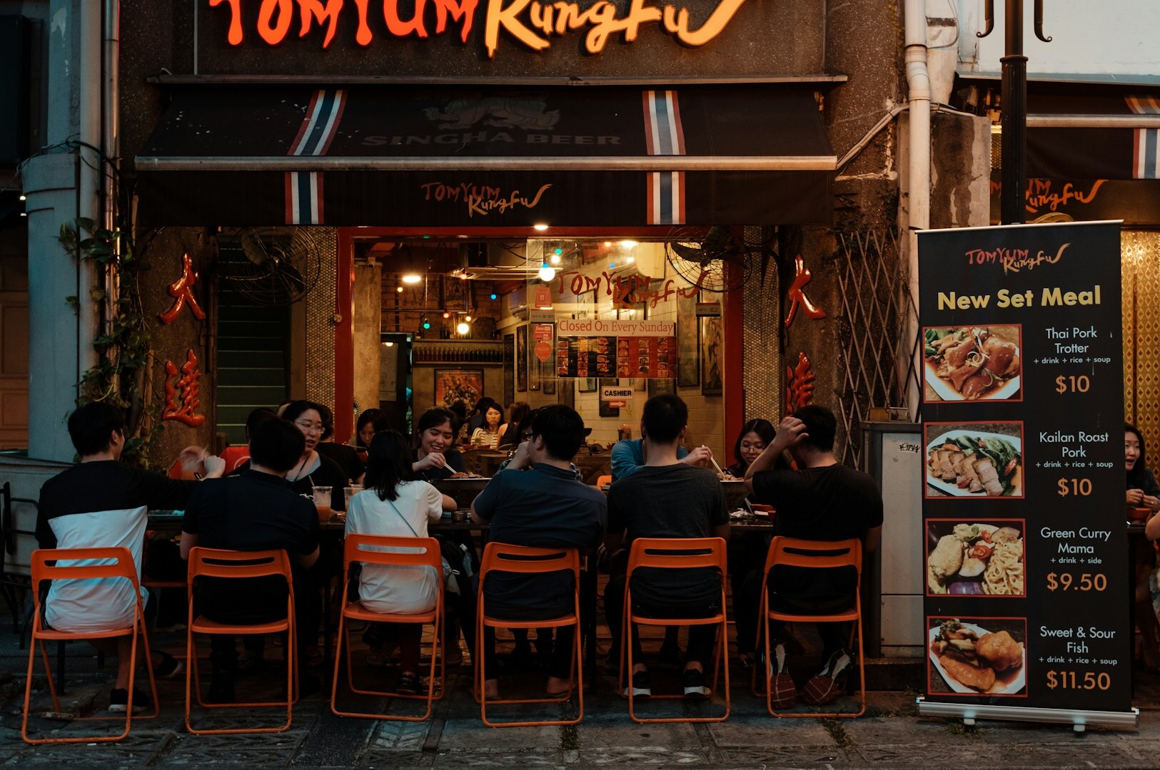 An exterior view of a restaurant in Singapore, showcasing a lively hawker center filled with diverse food options and patrons.