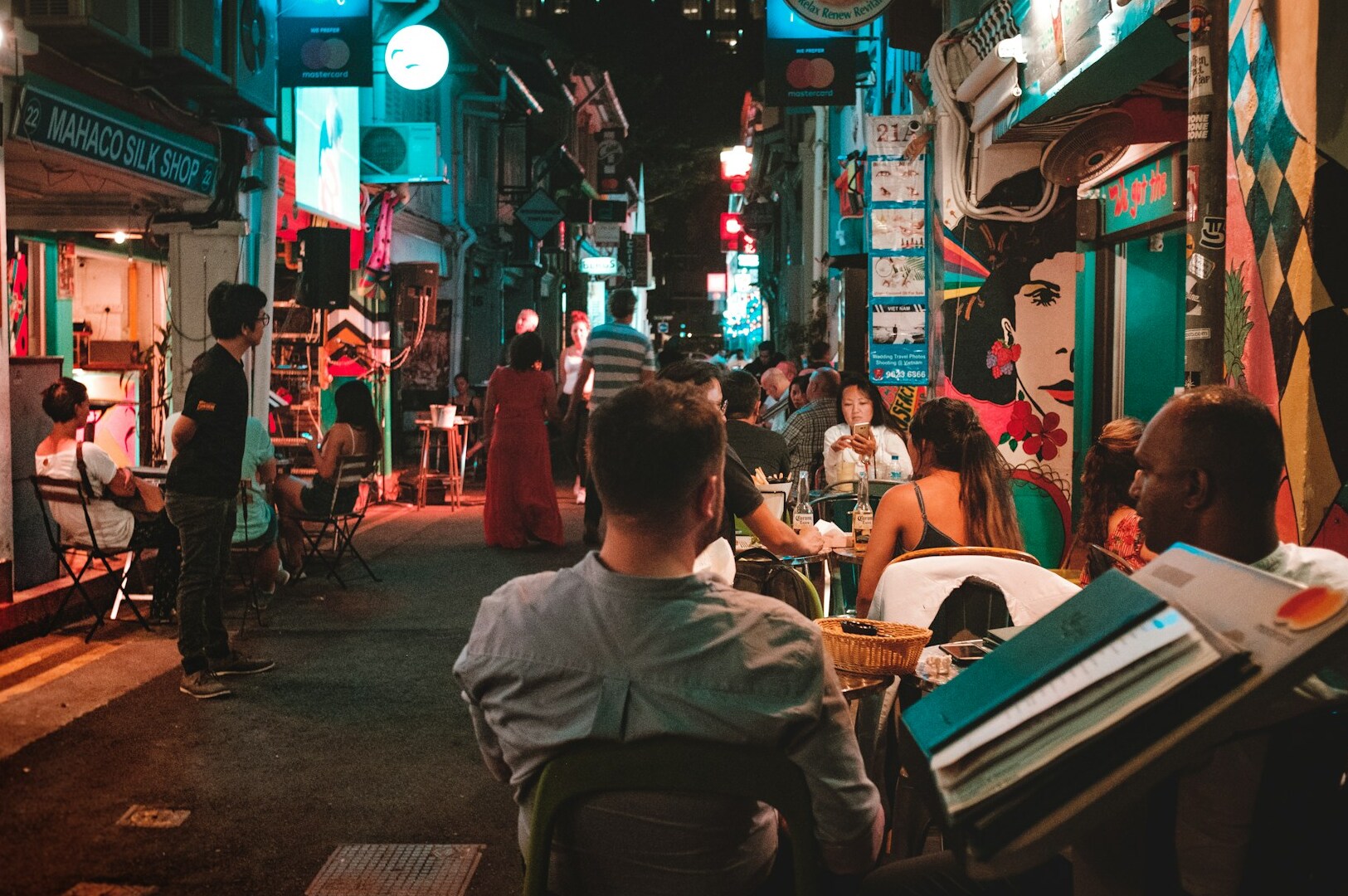 Nighttime scene of diners seated at tables in a narrow alley, experiencing the vibrant atmosphere.