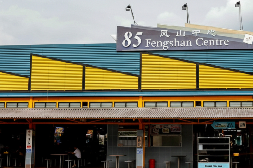 Exterior view of the 85 Fengshan Centre in Singapore, featuring a corrugated blue and yellow facade with its signature signage under a cloudy sky.