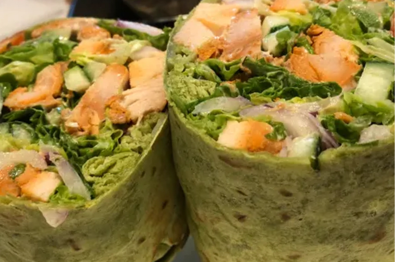 A close-up of two green spinach wraps sliced in half, packed with grilled chicken, fresh greens, onions, and cucumbers.