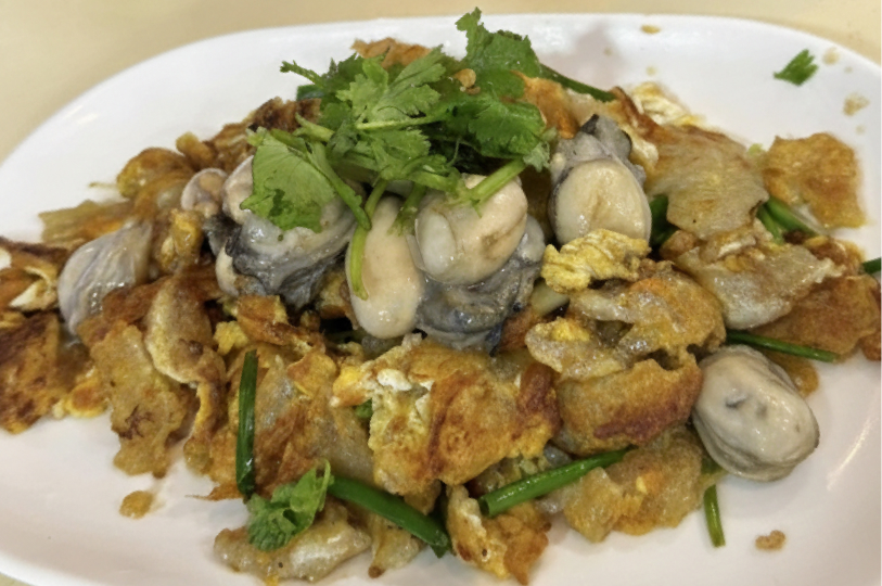 A plate of oyster omelette, featuring golden-brown fried egg and starch batter topped with several plump oysters and garnished with fresh cilantro.