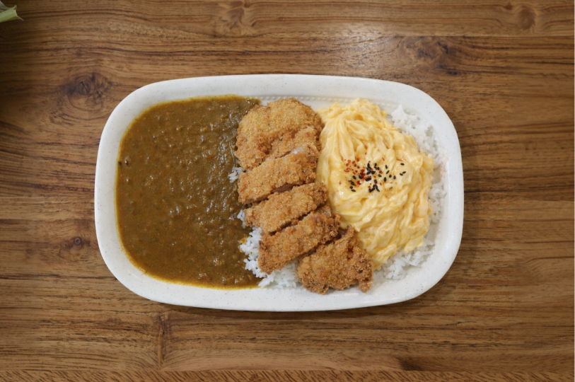 A top-down view of a white oval plate featuring Japanese curry, a sliced breaded cutlet (katsu), creamy scrambled eggs, and white rice.