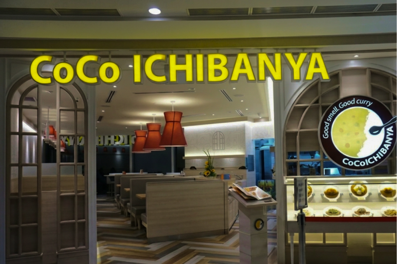 The storefront of a CoCo Ichibanya restaurant, showing the yellow logo and a display of plastic food models.