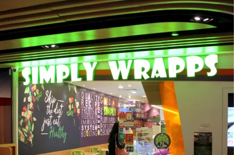 The bright green neon "Simply Wrapps" storefront sign with a wall graphic that says, "Skip the diet, just eat healthy."