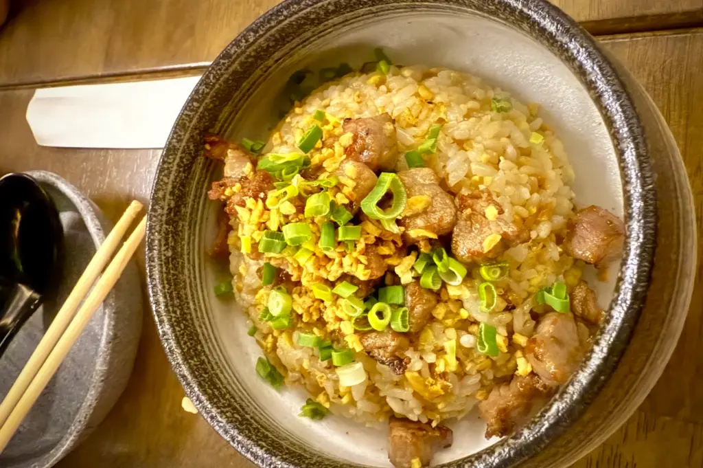 A fragrant bowl of Japanese garlic fried rice topped with tender cubes of seared wagyu beef and garnished with fresh spring onions, served in a rustic ceramic bowl at Ume San 100 in Singapore.