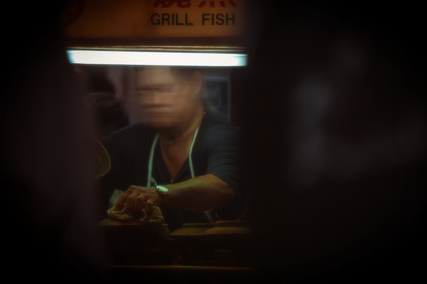A candid, blurry photo looking over a counter into a stall with an old sign above it that reads, "Grill Fish"