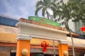 Entrance of Maxwell Food Centre in Singapore’s Chinatown district featuring the iconic hawker centre sign, tropical palm trees, traditional lantern decorations, and surrounding city skyline