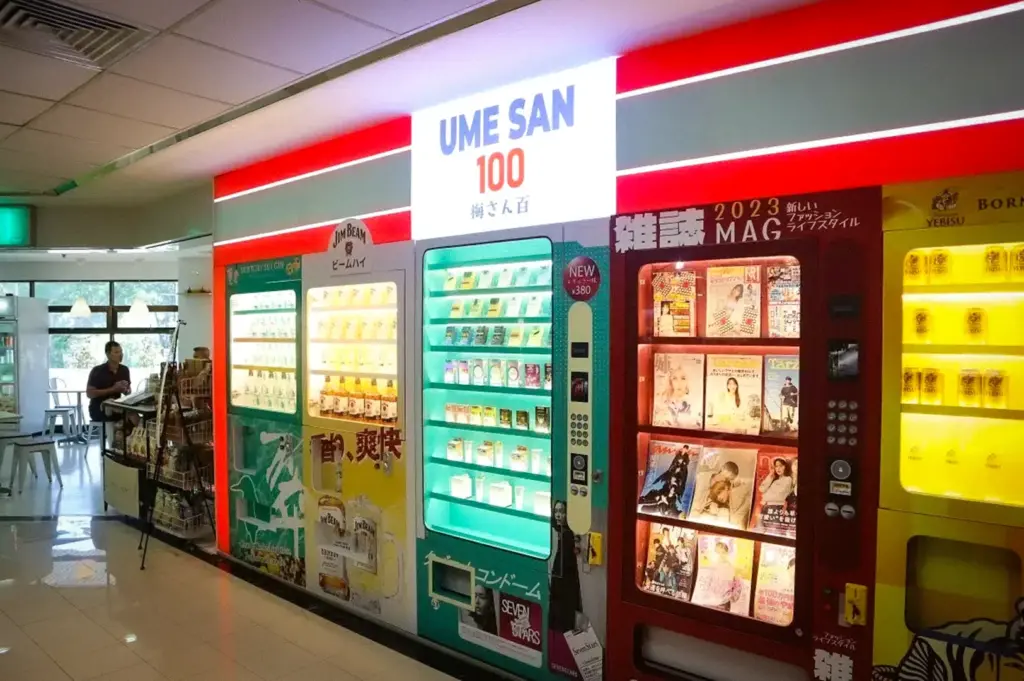 Colorful Japanese-themed vending machines and magazine dispensers inside UME SAN 100 in Singapore featuring drinks, snacks, and manga-style displays in a modern indoor space