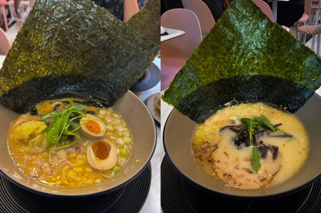 A side-by-side photo of two bowls of Japanese ramen served in dark bowls, each topped with a large sheet of roasted seaweed standing upright behind the noodles. The left bowl features soft-boiled eggs, corn, chopped onions, greens, and dumplings in a rich broth, while the right bowl contains creamy broth with mushrooms, greens, and slices of meat. Both dishes are presented on a restaurant table with pink chairs blurred in the background.