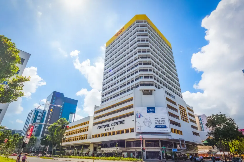 Exterior view of Fortune Centre in Singapore featuring the iconic yellow-topped high-rise building under a bright blue sky along a busy city street